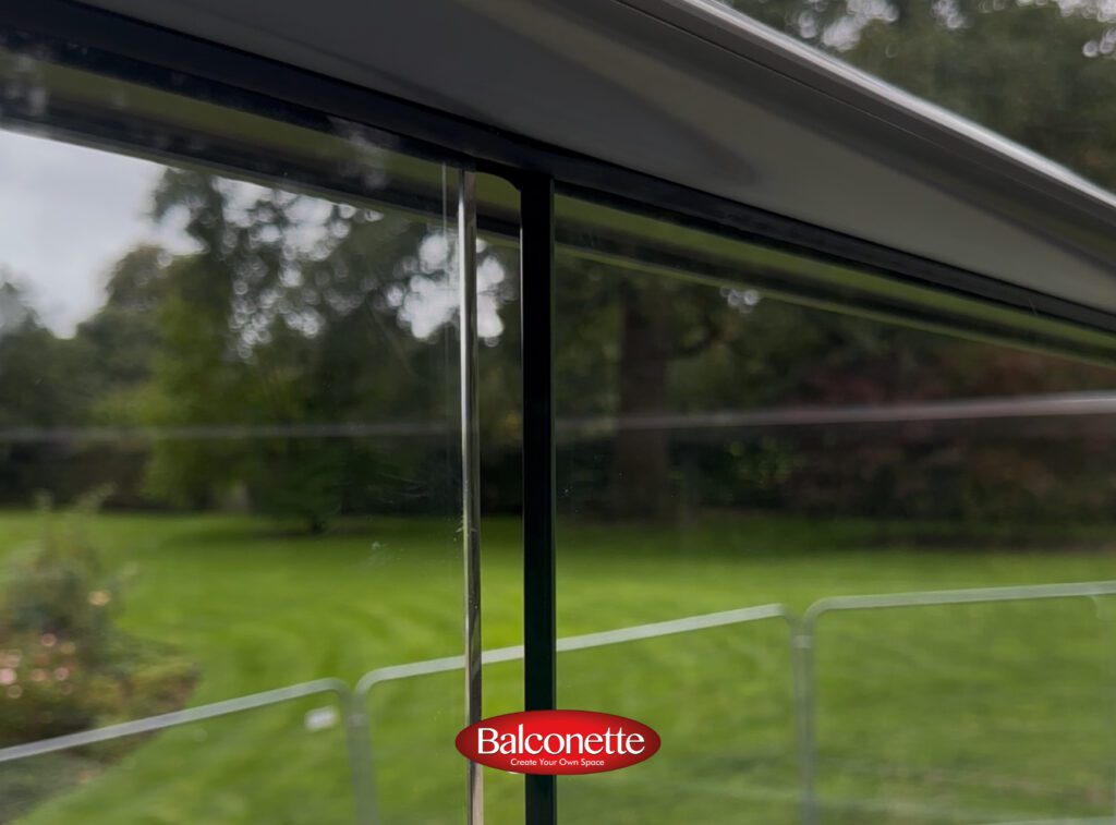 Close-up of the handrail and clear glass panels of a glass balustrade overlooking a garden